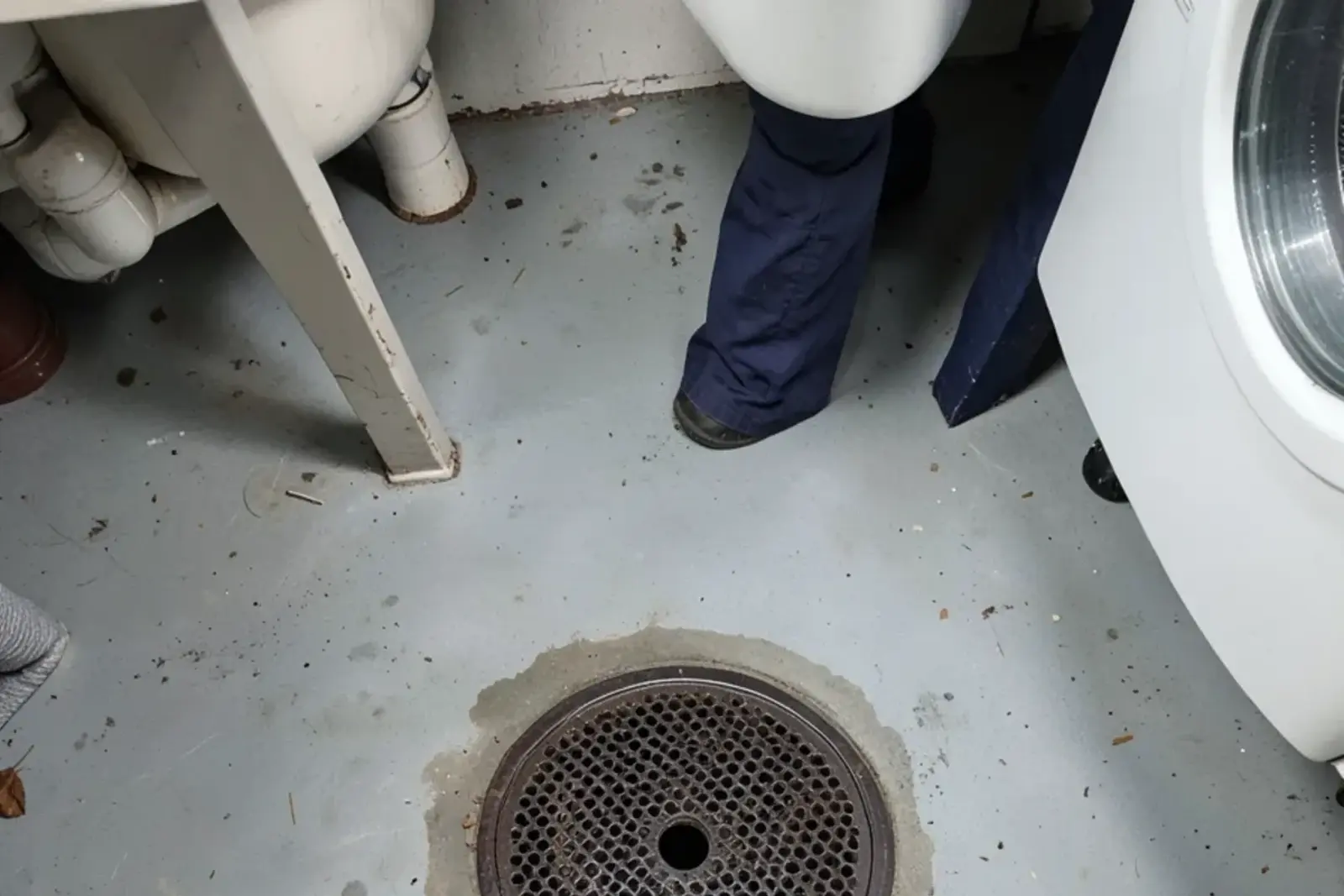 Round cast-iron floor drain set in an old painted concrete basement floor beside a laundry tub