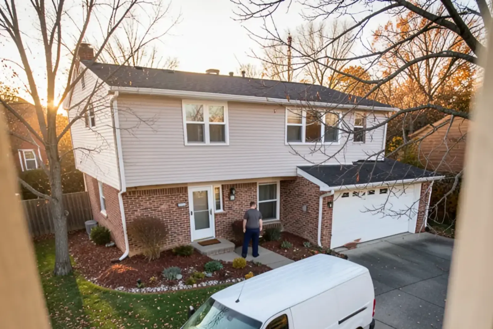 Tri-level brick and sided home with an attached garage and raked leaves on the lawn in late autumn
