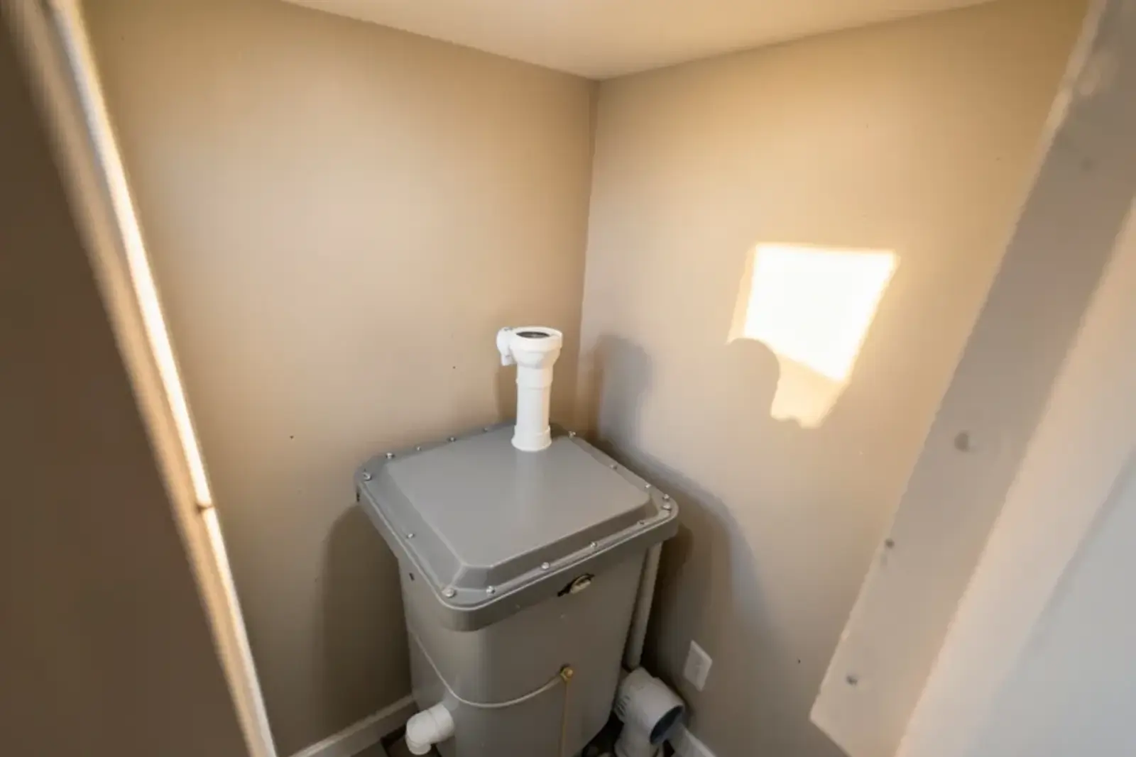 Sealed sewage ejector basin with a bolted lid, vent pipe and discharge pipe in the floor beside a basement bathroom wall