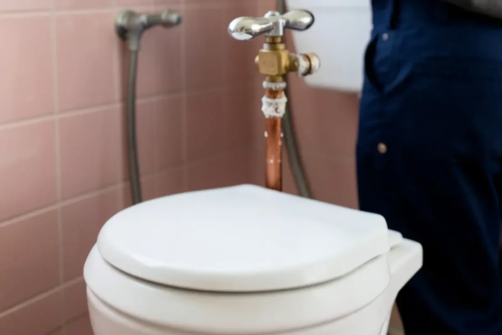 Old chrome multi-turn shutoff valve with mineral crust on the copper line behind a toilet tank